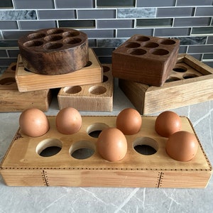 May include: A set of wooden egg holders, with one holder containing six brown eggs. The holders are made of natural wood and have a rustic look.
