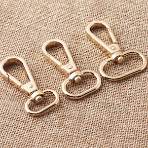May include: Three gold-toned metal clasps or hooks. The clasps are oval-shaped with a hook on one end and a loop on the other.