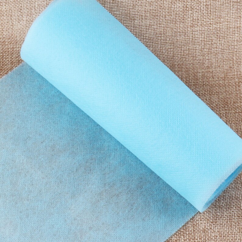 May include: A roll of light blue non-woven fabric. The fabric is unrolled and folded over on itself, showing the texture of the material.
