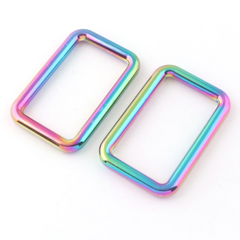 K&ouml;nnte beinhalten: Zwei regenbogenfarbene, metallische rechteckige Ringe mit irisierendem Effekt. Die Ringe sind glatt und gl&auml;nzend.