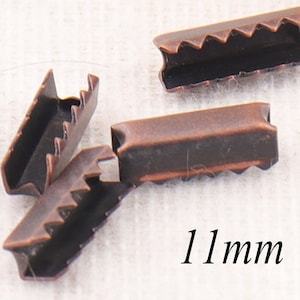 May include: Four antique copper-colored metal cord end stoppers, each measuring 11 mm in length. The stoppers have a serrated edge and a rectangular shape.