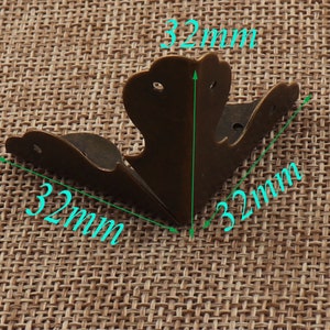 May include: Three antique brass corner protectors, each measuring 32 mm in length. The protectors have a decorative, ornate design.