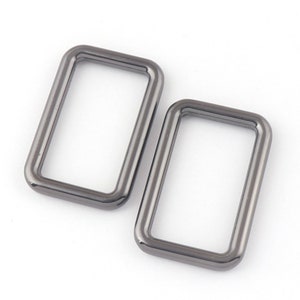 May include: Two silver-toned metal D-rings, each with a rectangular shape and a smooth, polished finish.
