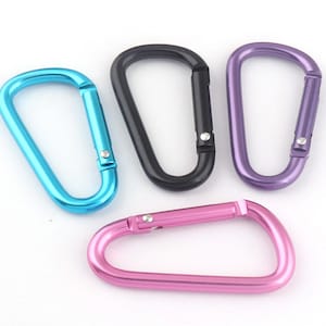 Puede incluir: Cuatro mosquetones de metal en diferentes colores: azul, negro, morado y rosa. Los mosquetones son todos del mismo tamaño y forma.