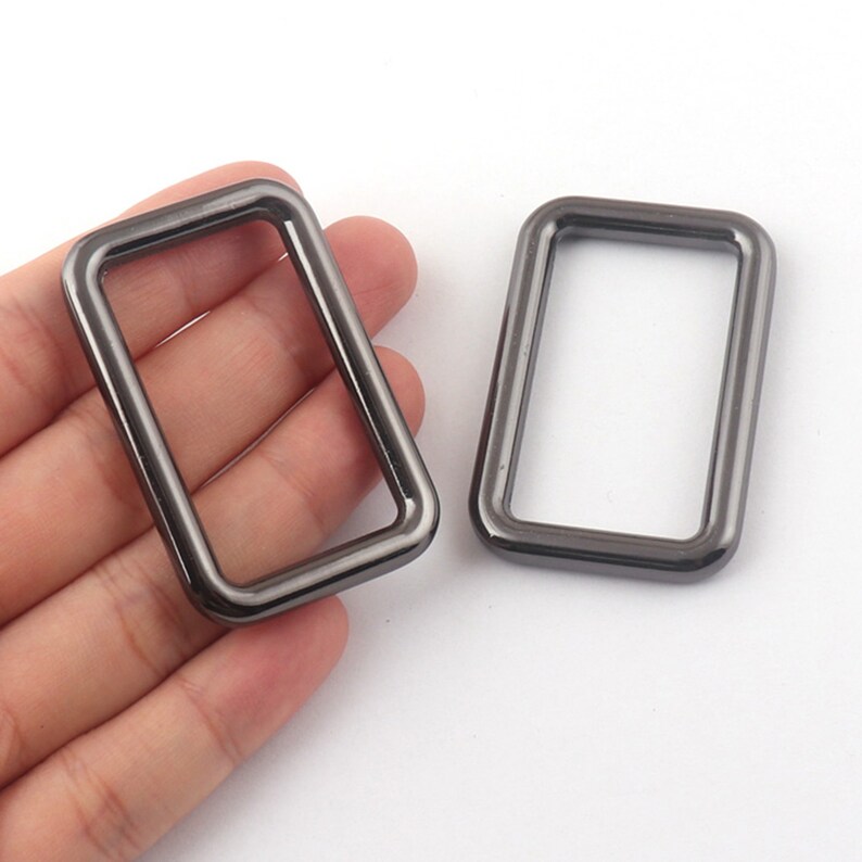 May include: Two gunmetal gray metal rectangular rings. The rings are smooth and have a polished finish.