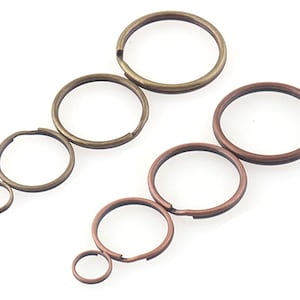Könnte beinhalten: Ein Satz mit sechs Schlüsselringen in zwei verschiedenen Größen und Ausführungen. Die größeren Schlüsselringe sind bronzefarben, während die kleineren kupferfarben sind.
