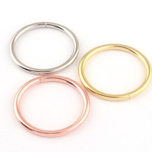 Puede incluir: Tres anillos de aro sin costuras en diferentes acabados metálicos: plata, oro y oro rosa. Los anillos son todos del mismo tamaño y están dispuestos en un semicírculo.