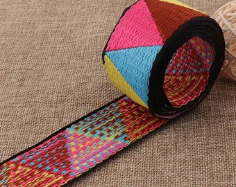 May include: A colorful woven fabric ribbon with a geometric pattern in shades of pink, blue, yellow, and brown. The ribbon is black edged and rolled up.