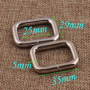 Op de afbeelding: Twee zilveren metalen D-ringen, een met een afmeting van 25 mm bij 29 mm en de andere met een afmeting van 35 mm bij 5 mm.