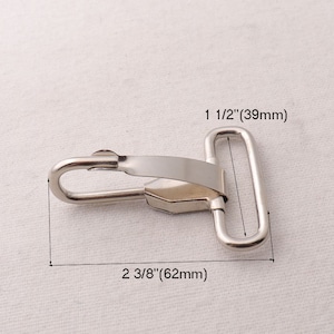 Könnte beinhalten: Silberner Metall-Schwenkhaken mit einer Öffnung von 39 mm Breite und einer Länge von 62 mm.