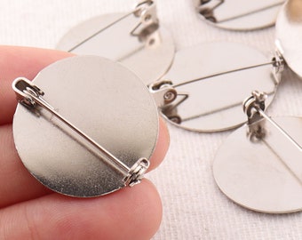 May include: A set of six silver-toned round metal blank brooch bases with a pin and catch closure. The bases are perfect for adding your own designs and embellishments.
