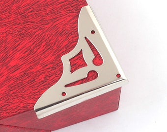 May include: Silver corner bracket with a decorative design. The bracket is attached to a red box.