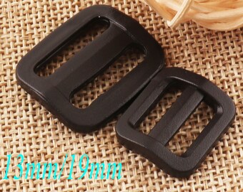 May include: Two black plastic slider buckles, one measuring 13mm and the other 19mm. The buckles are on a woven brown fabric background.