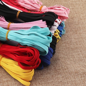 May include: A selection of colourful elastic bands in various colours, including black, white, pink, red, yellow, blue, and turquoise. The elastic bands are stacked on a brown hessian surface.