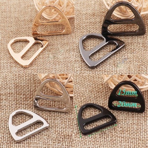 Op de afbeelding: Vier driehoekige metalen gespen in goud, zilver, zwart en gunmetal. De gespen hebben een ontwerp met dubbele lus en zijn verkrijgbaar in twee maten: 15 mm en 20 mm.