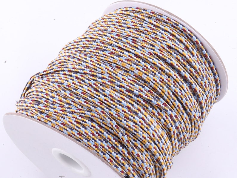 Op de afbeelding: Een spoel met veelkleurige koord met een witte achtergrond. Het koord is een mix van blauw, rood, geel en wit.