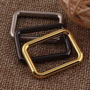 Puede incluir: Tres anillos en D de metal en diferentes acabados: dorado, plateado y negro. Los anillos están apilados uno encima del otro.