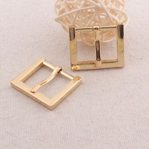 May include: Two gold-toned metal belt buckles. The buckles are square shaped with a smooth finish.