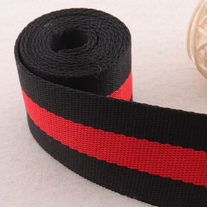 May include: Black and red striped webbing ribbon. The ribbon is rolled up and the red stripe is visible on the top.