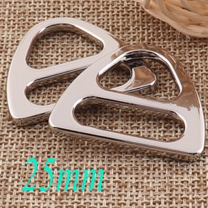 Op de afbeelding: Twee zilveren metalen D-ringen, elk met een driehoekige vorm en een afgeronde opening. De ringen hebben een diameter van 25 mm.