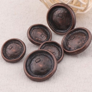 May include: Six antique bronze buttons with a square design in the center. The buttons are round and have a raised edge.