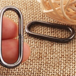 May include: Two silver metal oval rings, one held in a hand and the other lying on a woven brown surface.