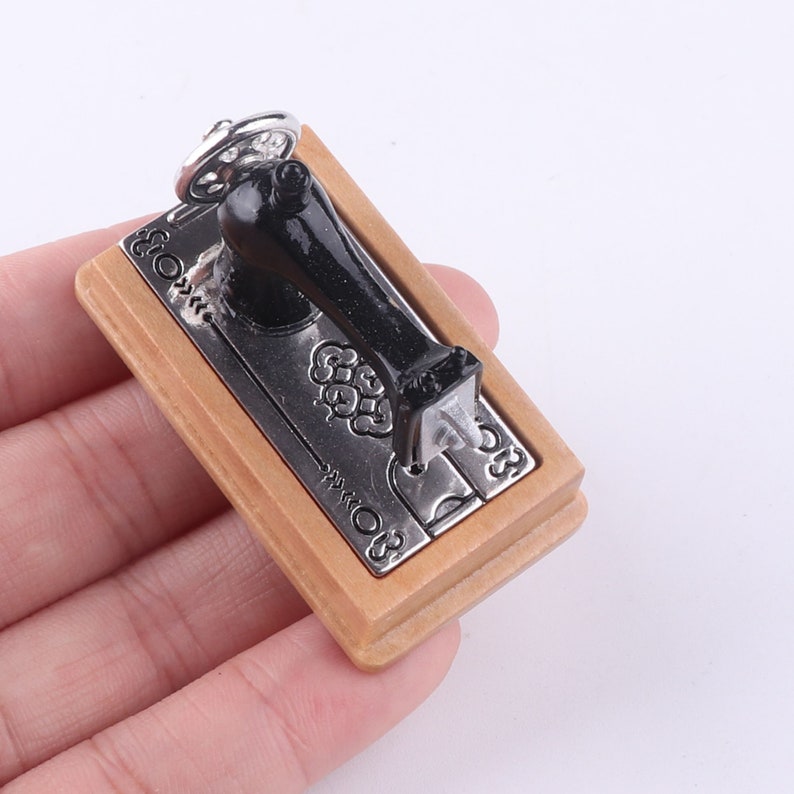 Może przedstawiać: Miniaturowy drewniany brelok w kształcie maszyny do szycia z czarną metalową maszyną do szycia i srebrnymi akcentami. Brelok ma napisane słowo "Szyć".