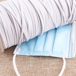 Puede incluir: Un rollo de cordón elástico blanco con una mascarilla quirúrgica azul sobre una superficie de tela marrón.