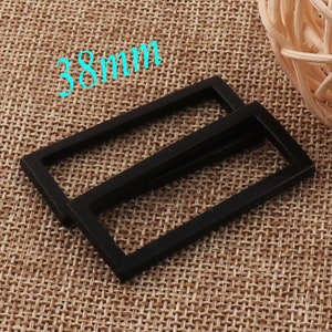 May include: Two black metal rectangular belt buckle frames, one on top of the other, on a brown woven fabric background. The text "38mm" is written in blue above the buckles.