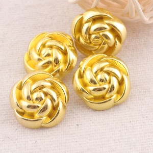 May include: Four gold-colored metal buttons shaped like roses. The buttons have a swirl design and a shiny finish.