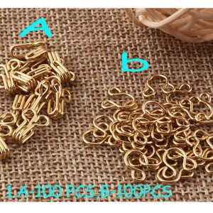 May include: Two piles of gold-colored metal clasps, labeled A and B.  100 pieces in each pile.  A-100 PCS, B-100PCS.