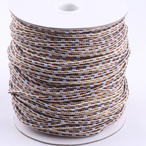 Op de afbeelding: Een spoel met veelkleurige koord met een witte achtergrond. Het koord is een mix van bruin, geel, blauw en wit.