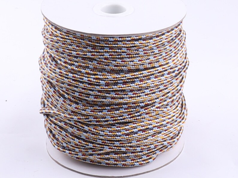 Op de afbeelding: Een spoel met veelkleurige koord met een witte achtergrond. Het koord is een mix van bruin, geel, blauw en wit.