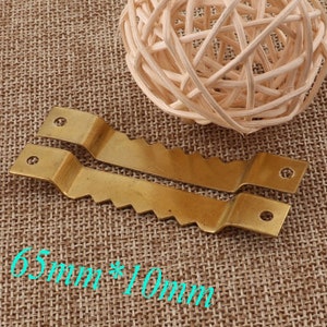May include: Two gold-colored metal picture hanging hooks with a serrated edge. The hooks are 6.5 cm by 1 cm.