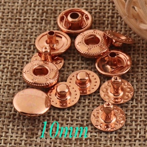 May include: A collection of 10mm copper-colored snap fasteners. The fasteners have a decorative design and are ideal for clothing, crafts, and other projects.