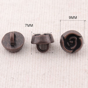 Może przedstawiać: Trzy antyczne brązowe guziki z wzorem róży. Guziki mają średnicę 7 mm i 9 mm.
