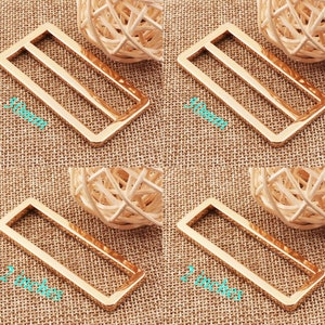 May include: Four gold-colored metal belt buckle slides in different sizes. The slides are rectangular with a single horizontal bar across the center. The slides measure 1 inch, 2 inches, 50mm, and 50mm.