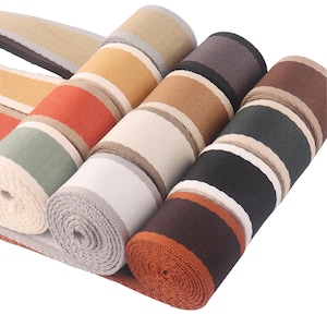 Puede incluir: Surtido de rollos de cinta de tela a rayas en varios colores, incluyendo marrón, negro, blanco, naranja y verde. La cinta está tejida con un patrón a rayas y es adecuada para manualidades, costura y decoración.