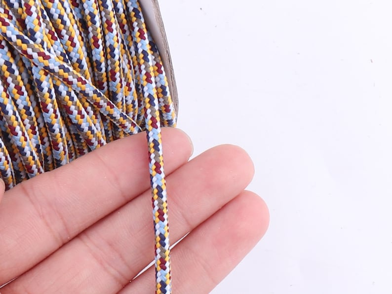Op de afbeelding: Close-up van een meerkleurig gevlochten koord met witte, blauwe, gele en bruine draden. Het koord wordt in een hand gehouden.