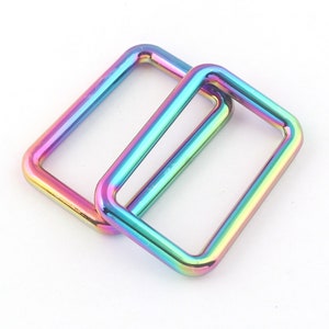K&ouml;nnte beinhalten: Zwei regenbogenfarbene D-Ringe aus Metall mit irisierendem Effekt. Die Ringe sind rechteckig und haben eine glatte, polierte Oberfl&auml;che.