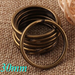 May include: A stack of 10 gold-toned metal key rings, each measuring 30mm in diameter. The key rings are arranged in a circle, with the top ring slightly offset from the others. The key rings are on a brown burlap background.