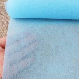 May include: A roll of light blue non-woven fabric. The fabric is soft and has a slightly textured surface.