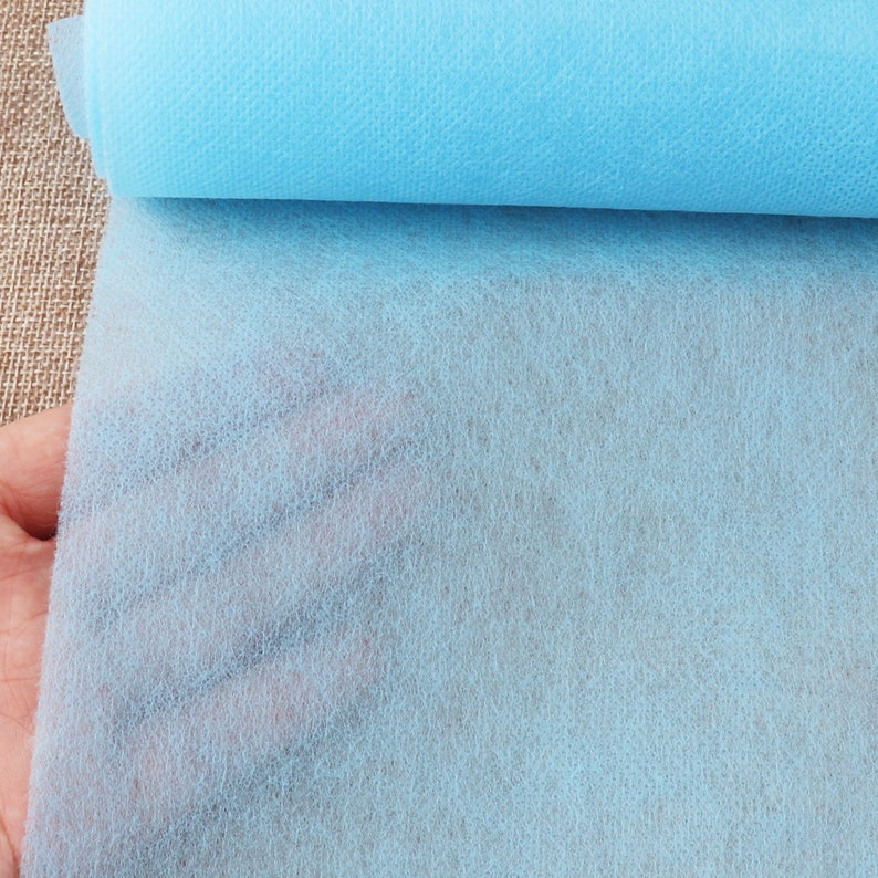 May include: A roll of light blue non-woven fabric. The fabric is soft and has a slightly textured surface.
