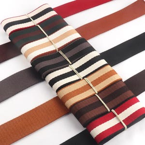Può includere: Assortimento di passamanerie a righe in vari colori, tra cui nero, bianco, marrone, rosso e beige. Il nastro è tessuto con un motivo a righe ed è perfetto per aggiungere un tocco decorativo a artigianato, abbigliamento e arredamento.