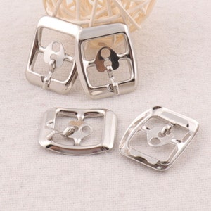 May include: Four silver-toned metal buckles with a rectangular shape and a centre opening. The buckles have a smooth, polished finish.