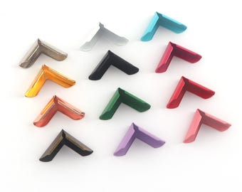 May include: Assortment of 12 corner protectors in various colors, including red, orange, yellow, green, blue, purple, black, and silver. These metal corner protectors are ideal for protecting the edges of paper, photos, and other crafts.