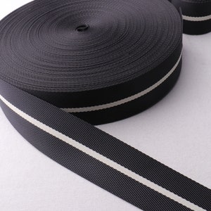 May include: Black webbing with a single white stripe running down the centre. The webbing is rolled up and the white stripe is visible on the edge.