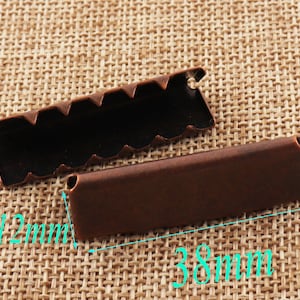 May include: Two antique copper-colored metal strap ends, one with a wavy edge and the other straight. The ends measure 38 mm long and 12 mm wide.