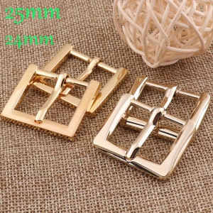May include: Two gold-toned metal belt buckles, one measuring 25mm and the other 24mm. The buckles are square shaped with a smooth, polished finish.