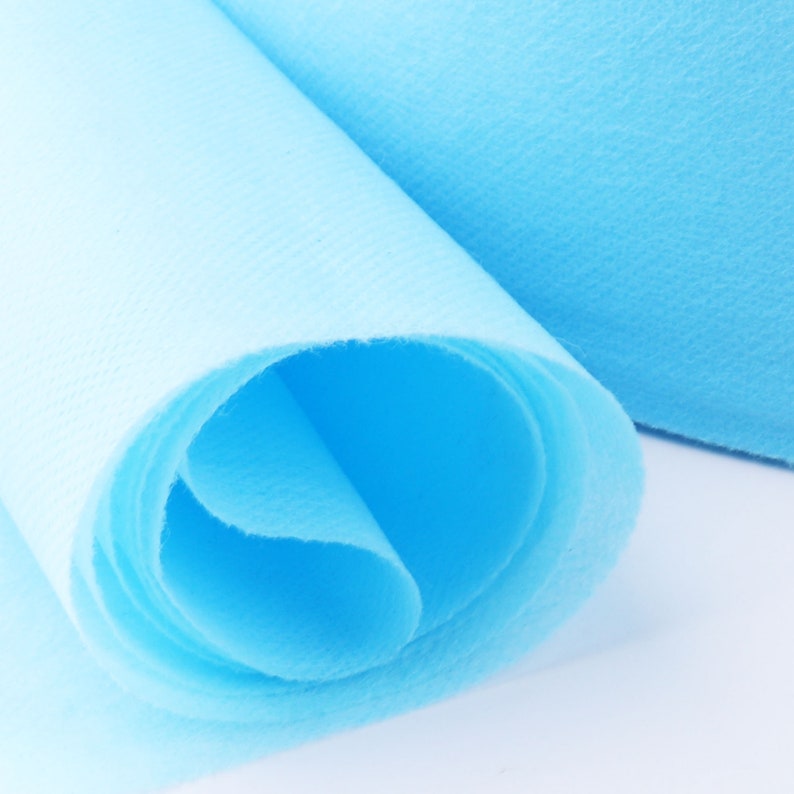 May include: A roll of light blue non-woven fabric, rolled up tightly. The fabric is soft and smooth, and it is perfect for a variety of craft projects.